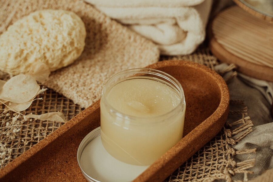 An open jar of balm on a cork tray with cream towels and a sponge