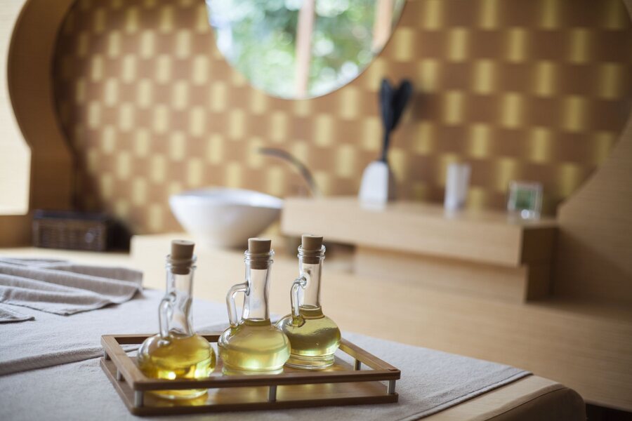 Massage oils in glass carafes on a bamboo tray, in a warm treatment room