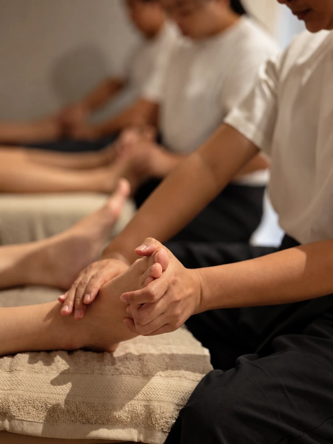 Therapists in white tops giving foot massages, a pair of hands holding a guest’s foot in front